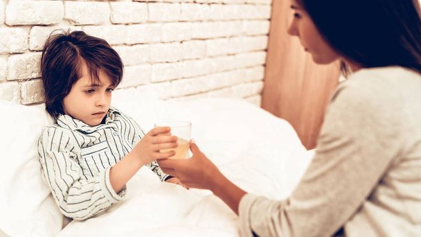 Mother Giving Medicine to Sick Son Lying Bed. Caring Mom Giving Sick Boy Pills. Worried Mother Giving Glass of Water to Ill Kid. Hospital Concept. Healthy Concept. Parent Concept. - Foto, Bild