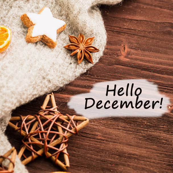 Winter theme. Spices, orange, cinnamon, anise, cookies in a shape of star, pepper, wooden stars and gray scarf on wooden background. View from above. Flat lay with text hello December. - Photo, Image