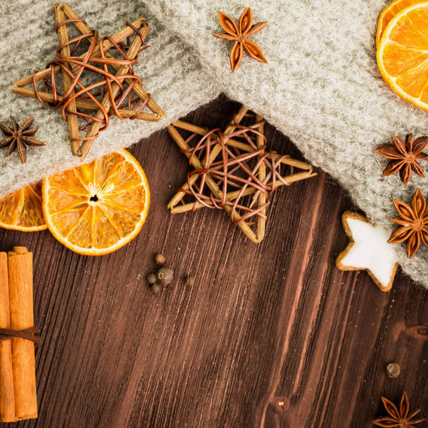 Winter and New Year theme. Spices, orange, cinnamon, anise, cookies in a shape of star, pepper, wooden stars and gray scarf on wooden background. Copy space for text. View from above. Flat lay. - Photo, Image