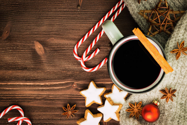 クリスマス ホット蒸しカップのきらめくワイングラスのスパイス、シナモン、アニス、星、赤いキャンデー、唐辛子と木製の背景にグレーのスカーフの形のクッキー。テキストのためのスペースにコピーします。上からの眺め。フラットを置く. - 写真・画像