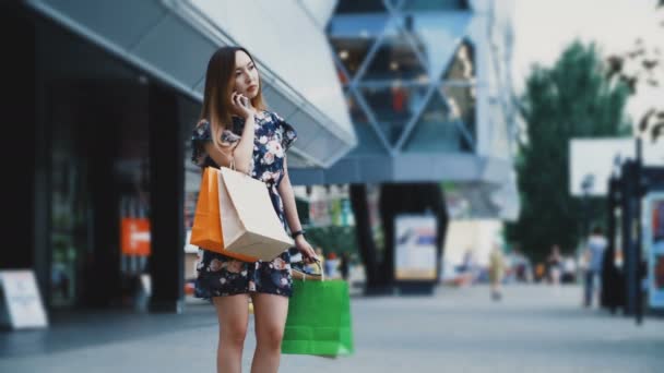 Kobieta z torbami na zakupy zamawia taksówkę w pobliżu centrum handlowego - Materiał filmowy, wideo