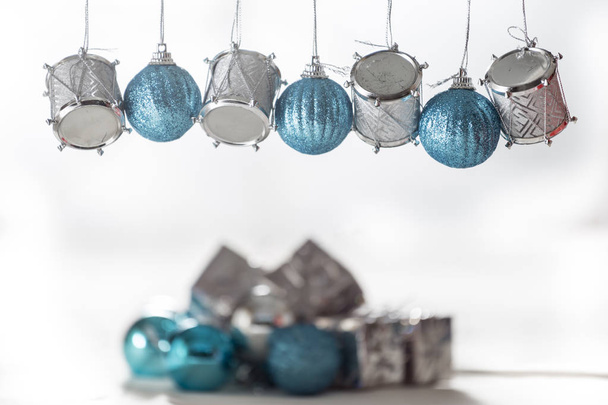 Christmas ornaments, silver drums and blue balls, hanging on a bar, on the floor a lot of defocused ornaments - Photo, Image
