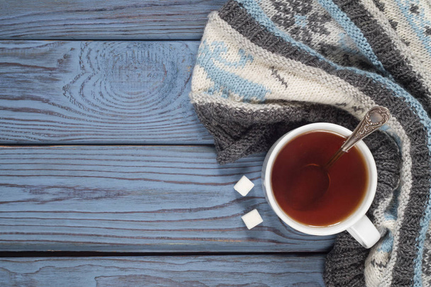 A cup of tea and a knitted scarf on the background of blue wooden table - Фото, зображення