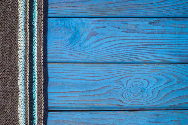 Fragment of a knitted scarf on blue wooden surface - Foto, imagen