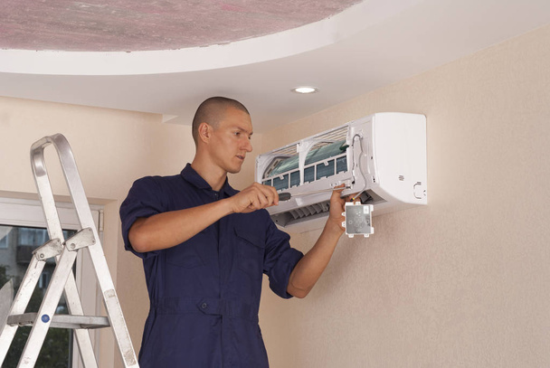 työntekijä asentaa sisäyksikön ilmastointilaitteen seinälle
 - Valokuva, kuva
