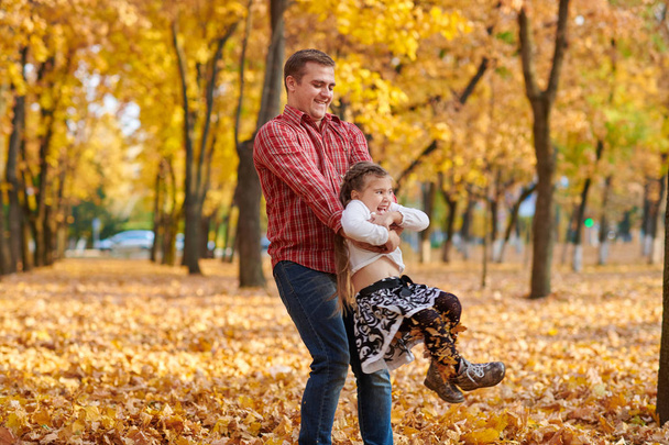 Padre e figlia stanno giocando e si divertono nel parco cittadino autunnale. Posano, sorridono, giocano. Alberi gialli brillanti
. - Foto, immagini