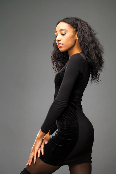 Молодая красивая африканская американка позирует в элегантном черном платье, снимок студии
. - Фото, изображение