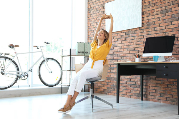 Beautiful young businesswoman stretching in office. Workplace fitness - Foto, afbeelding