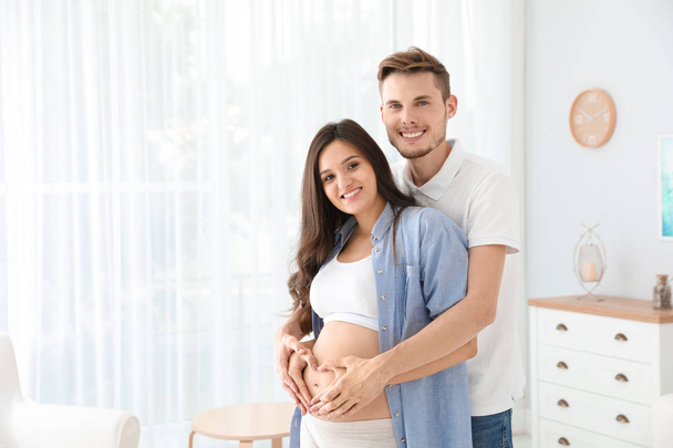 Pregnant woman and her husband showing heart with hands at home. Space for text - Foto, Imagem