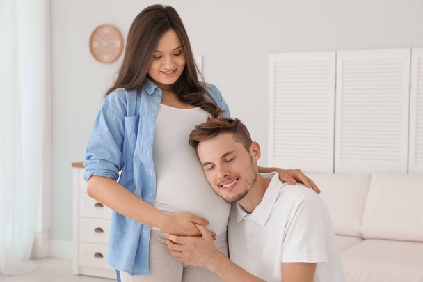 Young husband listening to his beautiful pregnant wife's tummy - Photo, image