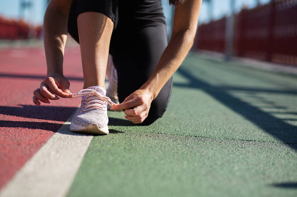 Jonge atleet vrouw koppelverkoop schoenveter op de atletiekbaan in zonnige dag. Ruimte voor tekst - Foto, afbeelding