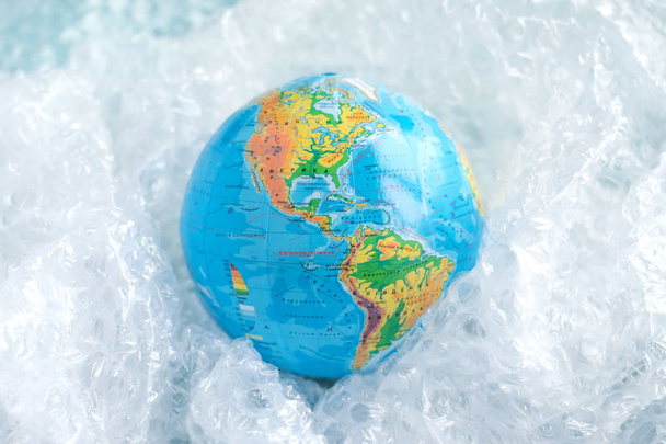 Physical globe, Earth in plastic wrap in carton box on blue background with copy space Recyclable packaging Ecology problem of environmental pollution planet by plastic Earth Day World Environment Day - Photo, Image