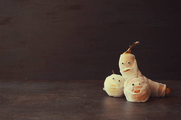 Halloween Fruit Mummy. Funny Scared orange, apple and banana with eyes and wrapped in bandages on dark background. Halloween DIY crafts. Ideas for festive decor - Photo, Image