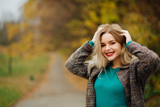 Joyful blonde woman in autumn coat posing near the yellow trees. Space for text - Photo, Image