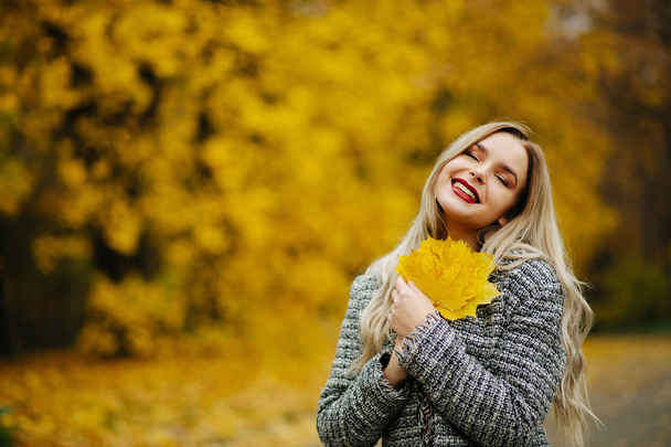Cheerful blonde woman in autumn coat holding autumn yellow maple leaves. Space for text - Valokuva, kuva