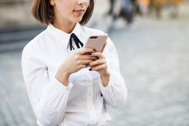 Portrait of a beautiful woman using mobile phone while standing on blurred street background. Girls using an application in her smart phone. - Φωτογραφία, εικόνα