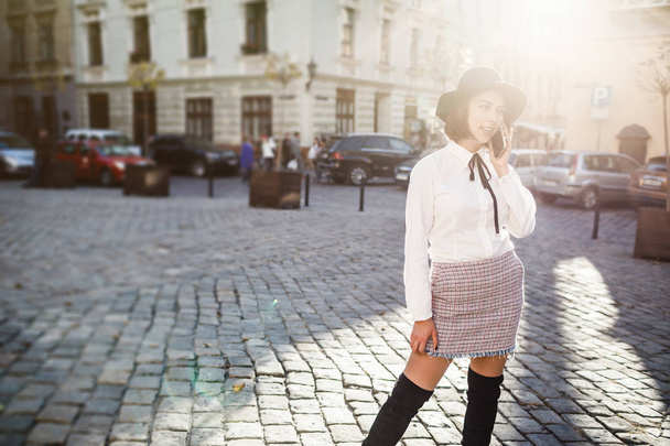 Portrait of a beautiful woman using mobile phone while standing on blurred street background. - Фото, изображение
