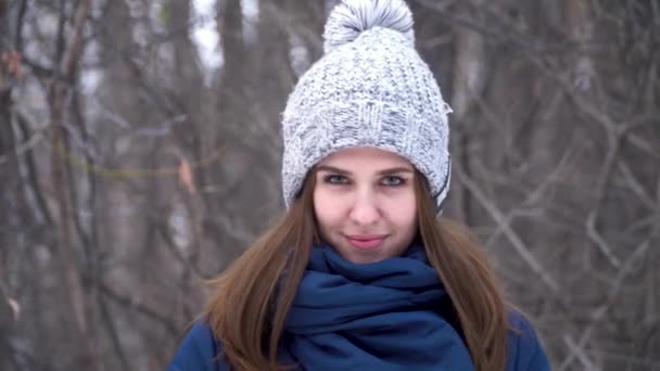 Retrato de cerca de la hermosa joven mujer caucásica sonriente en chaqueta de invierno, sombrero y bufanda. Chica morena retrato de madera nevada
 - Metraje, vídeo