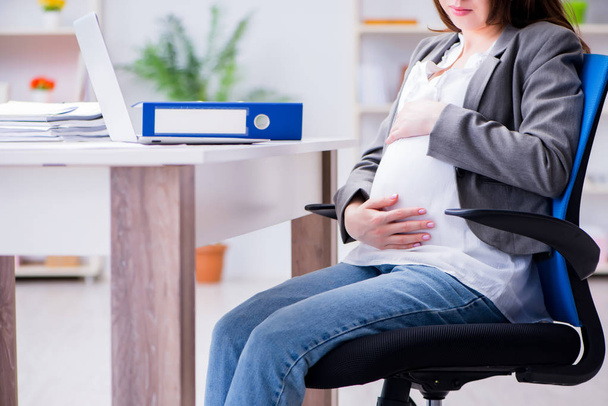 Mulher grávida lutando com dor no escritório
 - Foto, Imagem