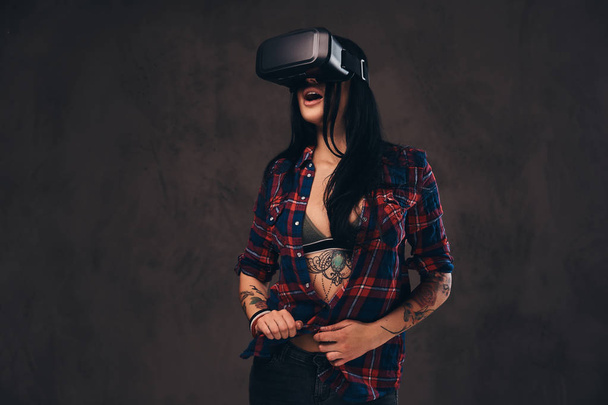 Tattooed girl wearing a red unbuttoned checked shirt wearing a VR headset. - Photo, Image