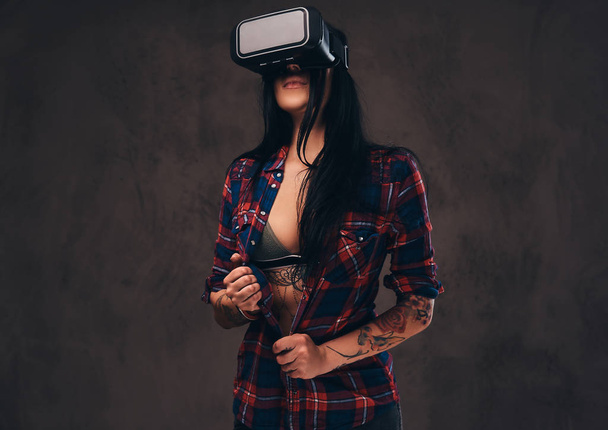 Chica tatuada con una camisa a cuadros desabotonada roja con auriculares VR
. - Foto, imagen