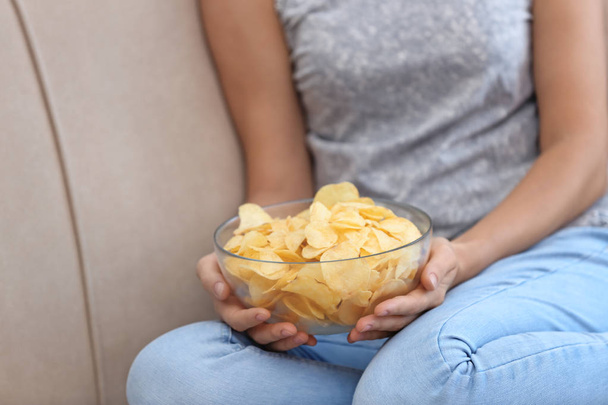 Жінка з чашкою картопляних чіпсів сидить на дивані, крупним планом
 - Фото, зображення