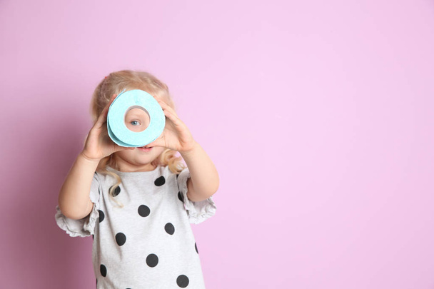 Cute little girl looking through toilet paper roll on color background. Space for text - Photo, Image