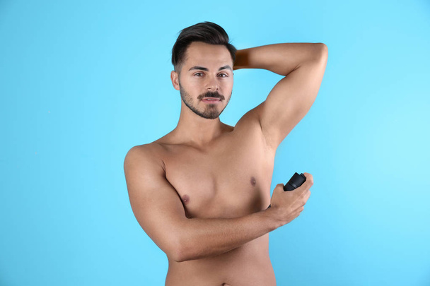 Young man using deodorant on color background - Фото, зображення