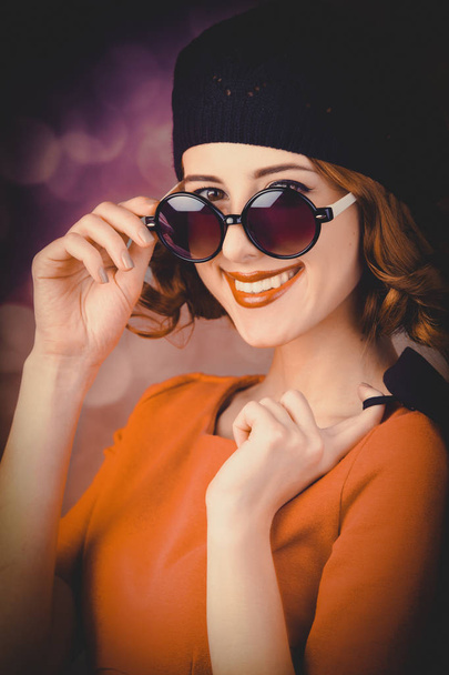 ritratto di una bella ragazza con i capelli ricci vestita con un berretto e occhiali da sole su uno sfondo grigio
. - Foto, immagini