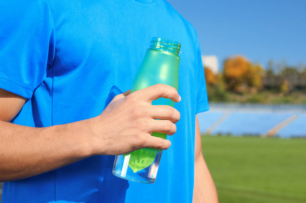 Sporty man holding bottle of water at stadium on sunny day, closeup - Foto, afbeelding