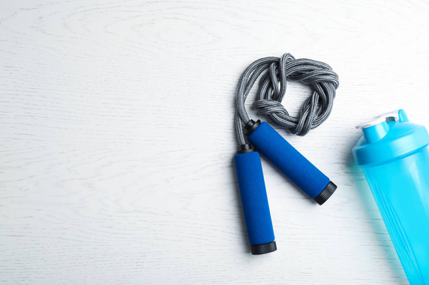 Jump rope, bottle of water and space for text on white wooden background, top view - Foto, immagini
