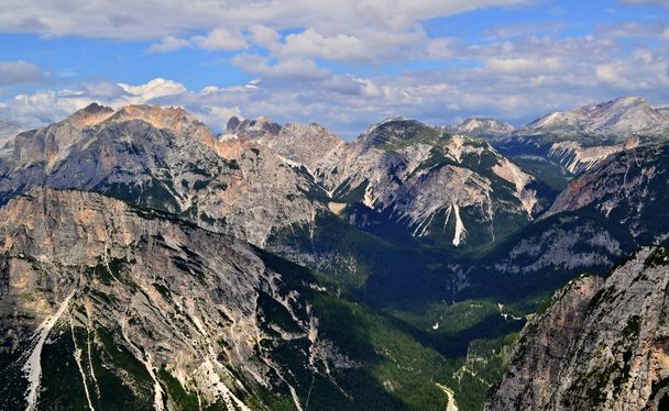 пики итальянских Альп - Доломиты, освещенные солнцем. Зеленый лес находится в долинах под горами, частично облачно небо с голубыми пробелами над горами. Посмотри с пика Пунта Файмс. Альпы, Италия, лето 2018 года
 - Фото, изображение
