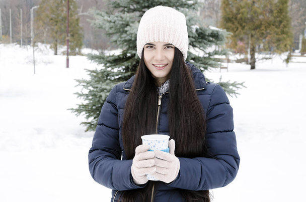 young girl holding thermo cup with hot drink sitting on a bench, winter cold day - Valokuva, kuva
