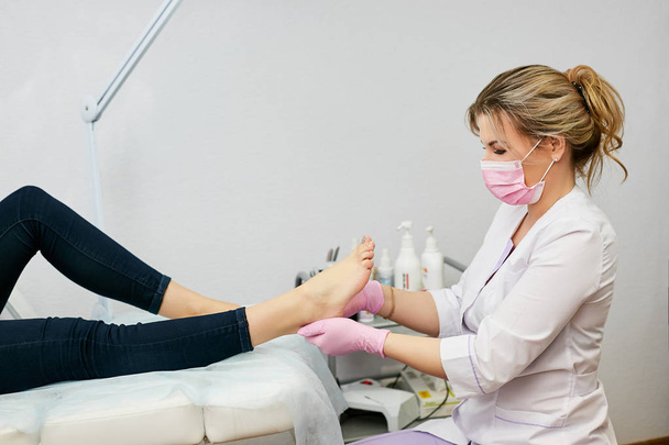Pedicure specialist in the beauty salon performs the work of caring for the feet of a young girl - Φωτογραφία, εικόνα