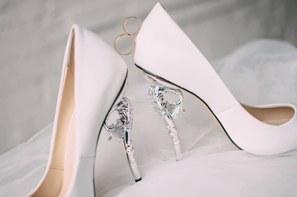 A pair of white wedding shoes with rings on a stool. - Photo, Image