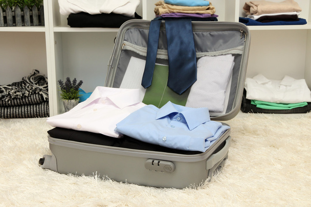 Open grey suitcase with clothing in room - Фото, изображение