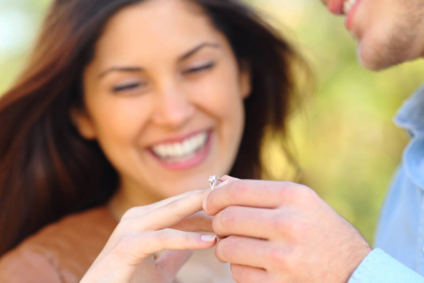 Happy man putting engagement ring to his glad girlfriend after proposal outdoors in a park - Foto, Imagen