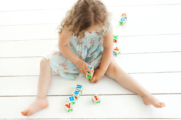 Симпатична маленька дівчинка грає з кубиками абб. Дитина навчається на нейтральному фоні
 - Фото, зображення