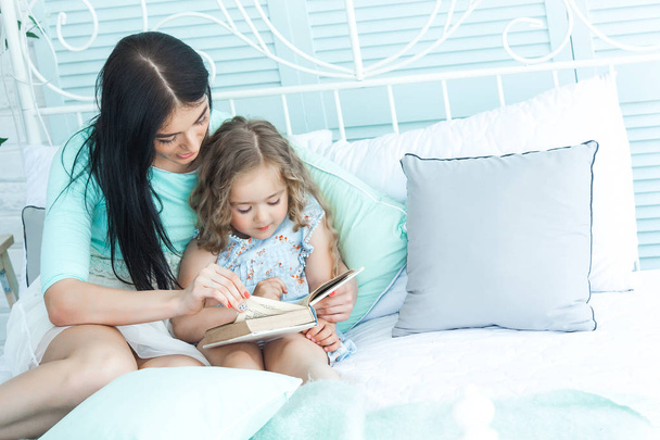 Νεαρή μητέρα διαβάζοντας ένα παραμύθι για τη μικρή της κόρη υπνηλία - Φωτογραφία, εικόνα