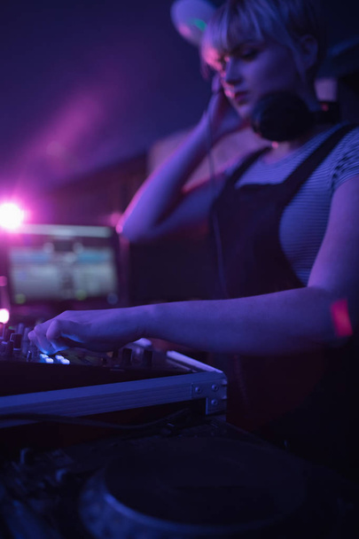 Женщина ди-джей слушает наушники, играя музыку в баре
 - Фото, изображение