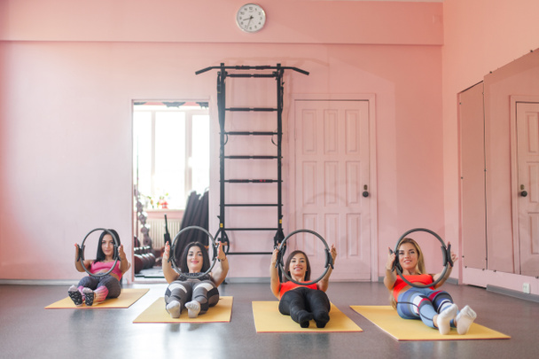 Groep jonge vrolijke vrouwen maken van pilates oefeningen met fitness ringen - Foto, afbeelding