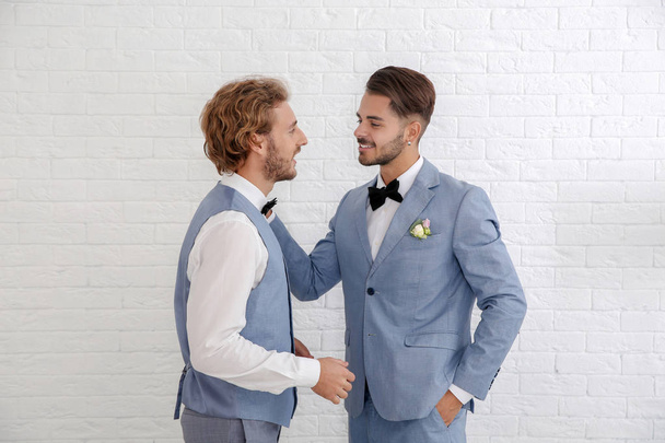 Happy newlywed gay couple in suits against white wall - Фото, зображення