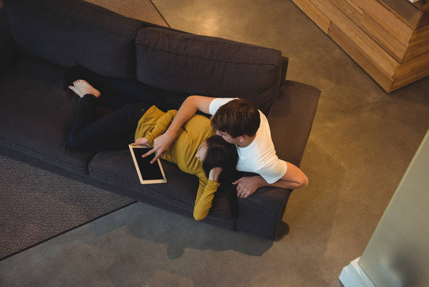 Veselý pár leží vedle sebe na pohovce pomocí digitálních tabletu v obývacím pokoji - Fotografie, Obrázek