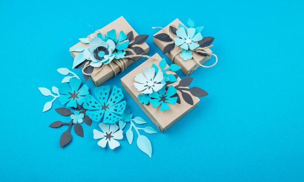 Gift box wrapped in craft paper blue background. Sakura flower made from paper origami. Present. - Foto, Imagen