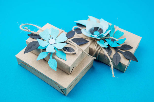 Gift box wrapped in craft paper blue background. Sakura flower made from paper origami. Present. - Photo, image
