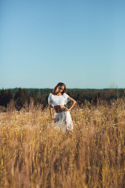 眺めること若い女の子 croppet のトップと白のリネン パンツ立っている夕焼け草原でポーズをとって - 写真・画像