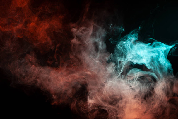 Πολύχρωμα καπνός από ένα vape πράσινο και κόκκινο χρώμα του περίεργο μυστικιστική φόρμα σε μαύρο φόντο απομονωμένες. Φωτεινά σύννεφα σε αφηρημένη μορφή. - Φωτογραφία, εικόνα