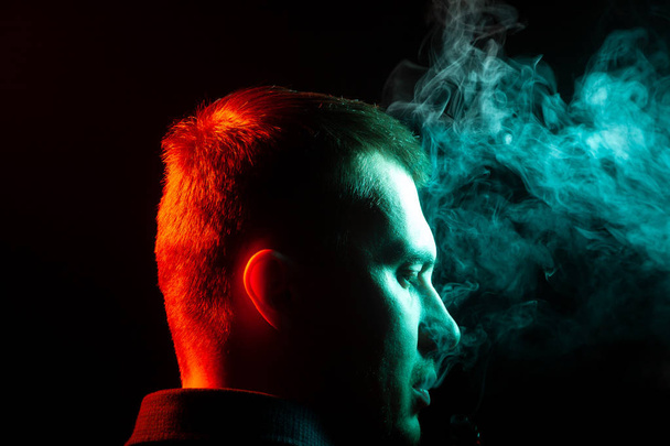 A view from the back of a mans head around in a shirt smoking and exhaling multi-colored smoke of green to different sides from himself on a black isolated background.  - Fotoğraf, Görsel