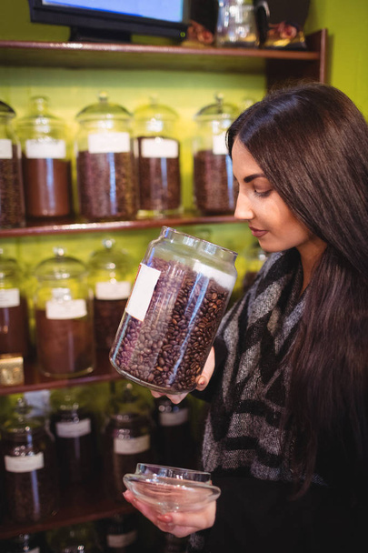 Krásná žena vonící sklenice kávová zrna v obchodě - Fotografie, Obrázek