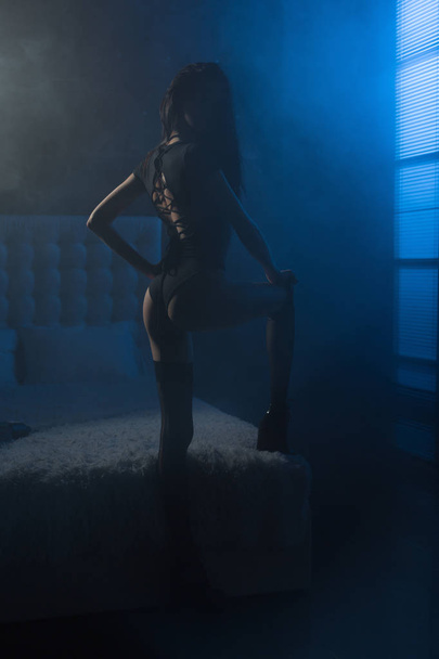 Beautiful young woman in a sexy witch costume and torn stockings getting ready to halloween party in her bedroom full of fog and moonlight trough window. - Foto, immagini